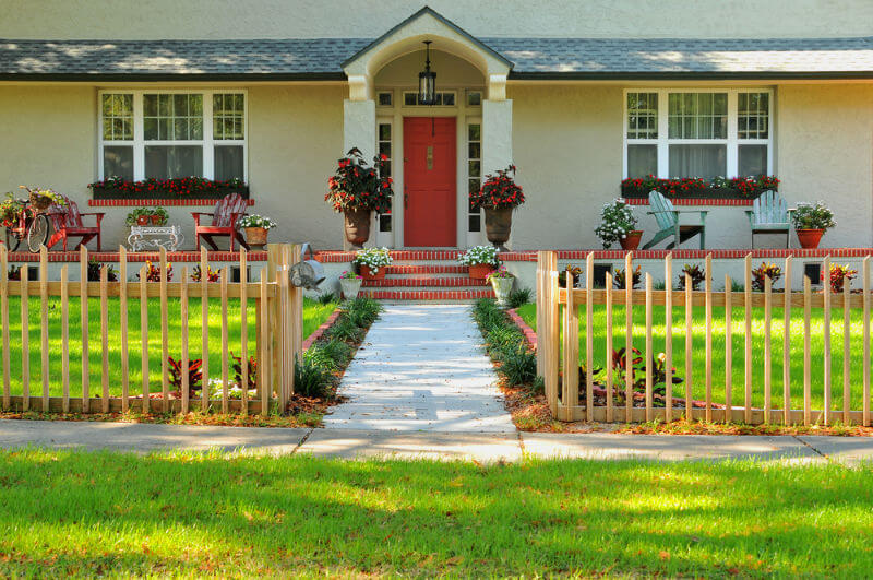 entryway of a nicely kept home with paved walkway, columns,decorative fence and beautiful landscaping