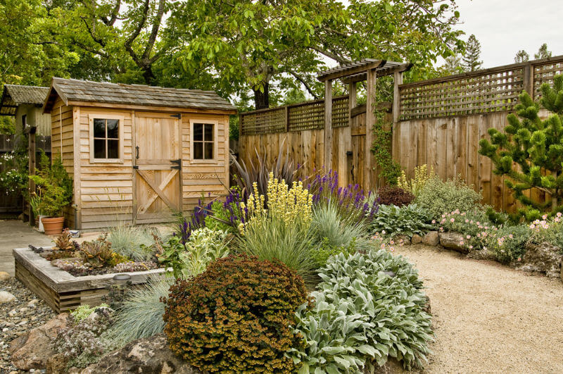 landscaped backyard with lattice top fence, small wood shed, and pathway